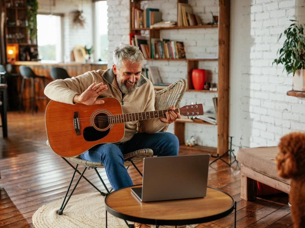 Ett barn sitter vid ett soffbord och gör läxor medan en vuxen spelar gitarr i ett färgglatt vardagsrum.