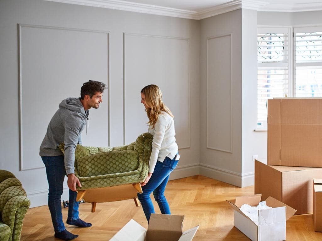 Two people carrying a sofa with boxes L