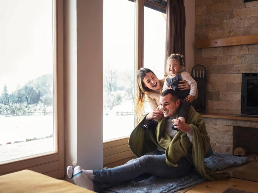 En kvinna och ett barn sitter vid ett stort fönster i vintermiljö, inlindade i filtar.